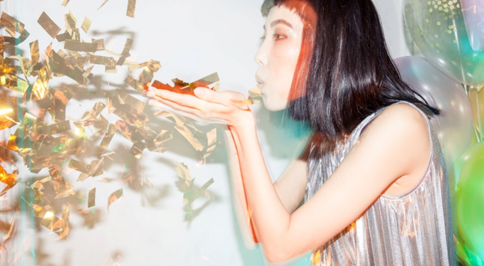  Asian woman wearing silver shiny dress and blowing gold confetti